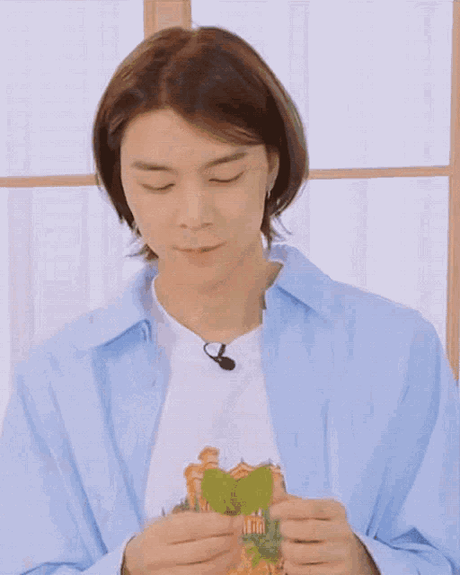 a man in a blue shirt is holding a green leaf in his mouth