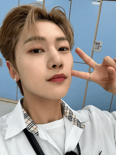 a young man wearing a white shirt and plaid collar is making a peace sign