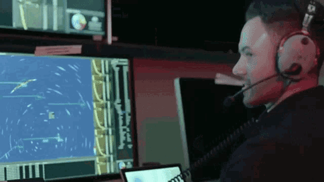 a man wearing headphones and a microphone looks at a computer monitor