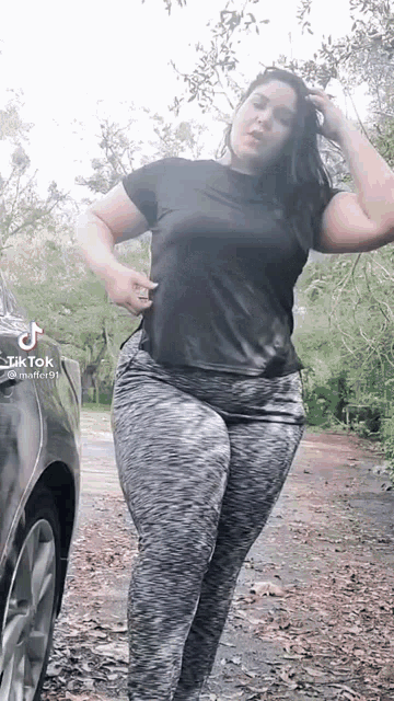 a woman in a black shirt and gray leggings is standing next to a car .