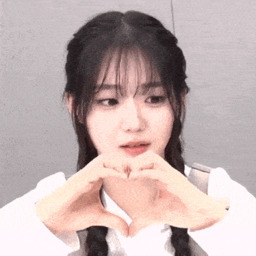 a young girl with braids is making a heart shape with her hands .