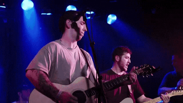 a man singing into a microphone while another man plays guitar on stage