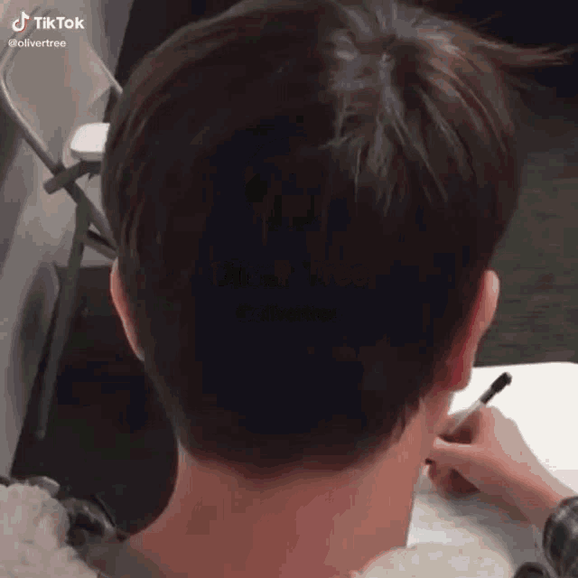 the back of a person 's head is shown while they write on a piece of paper with a pen .