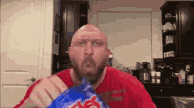 a bald man in a red shirt is eating chips