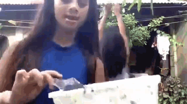 a girl in a blue top is holding a piece of plastic in her hand .