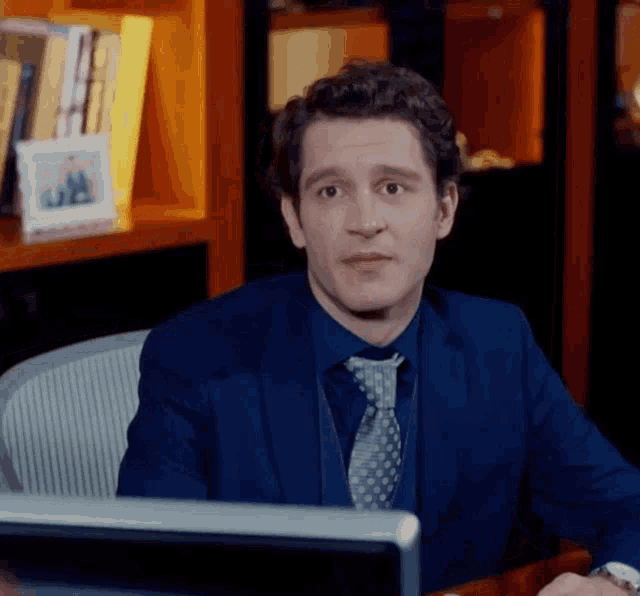 a man in a suit and tie sits at a desk in front of a computer