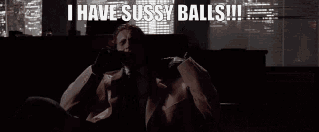 a man in a suit and tie is sitting on a couch and says i have sussy balls .