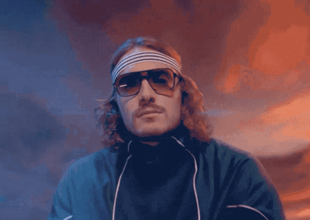 a man wearing sunglasses and a headband is sitting in front of a sign that says ologia