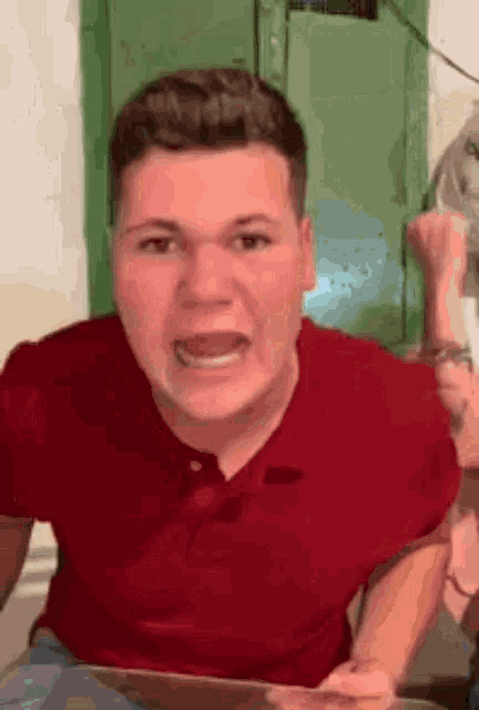 a young man in a red shirt is making a funny face .