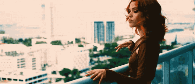 a woman stands on a balcony looking out over a city