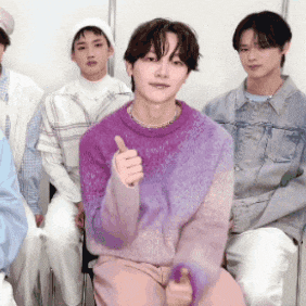 a man wearing a purple sweater is giving a thumbs up sign