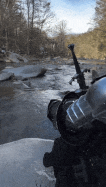 a person holding a sword in front of a river with trees in the background