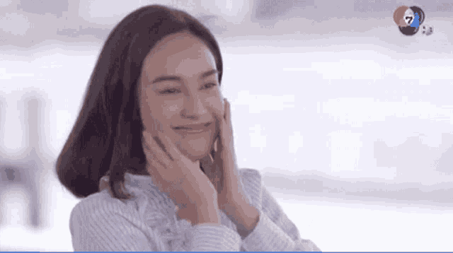 a woman is smiling and touching her face with her hands while wearing a striped shirt .