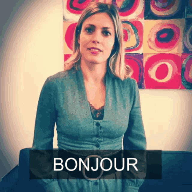 a woman stands in front of a colorful painting and says bonjour