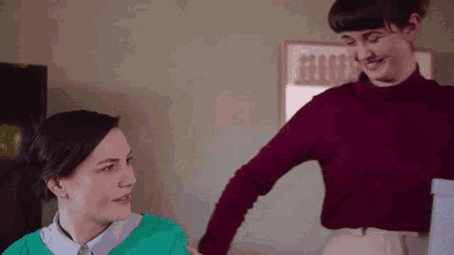 a woman in a green sweater is standing next to another woman in a burgundy sweater