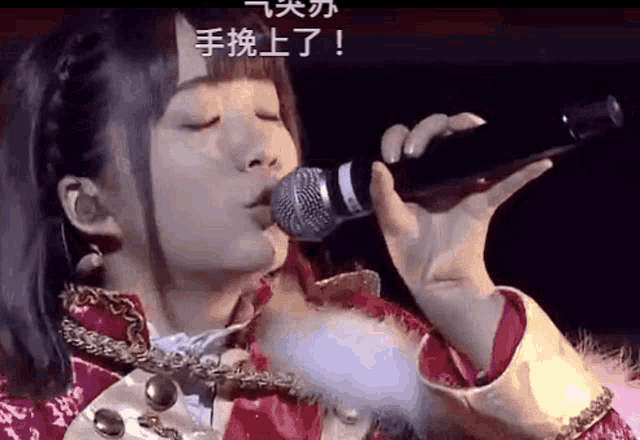 a woman singing into a shure microphone with chinese writing on the screen behind her