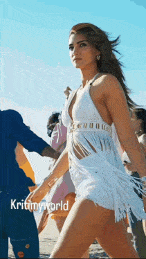 a woman in a white dress with fringe is walking on the beach