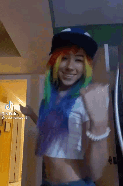 a girl with rainbow hair is wearing a hat and smiling