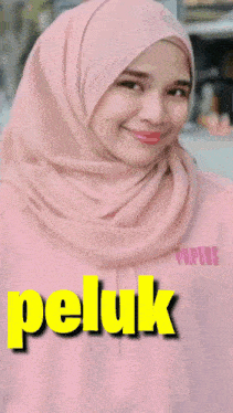 a woman wearing a pink hijab with the words peluk aku on the bottom right