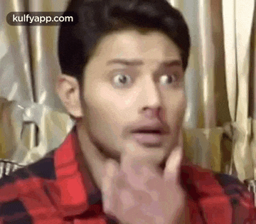 a man in a red and black plaid shirt is making a funny face with his hand .