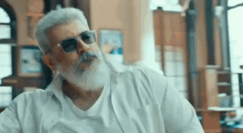 a man with a beard and sunglasses is smoking a cigarette in a living room .