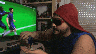 a man wearing sunglasses and a red hat is watching a soccer game