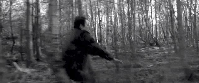a man in a black jacket is running through a dark forest .