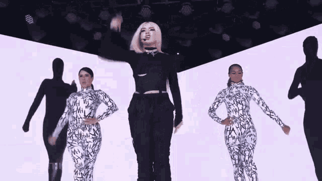 a woman in a black and white jumpsuit is standing in front of a group of women in white and black jumpsuits .