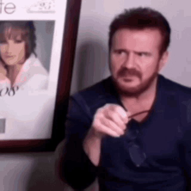 a man with a beard is sitting in front of a picture of a woman .