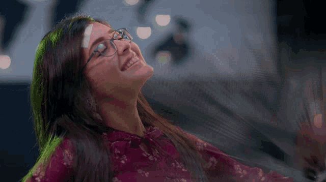 a woman wearing glasses and a purple top is smiling
