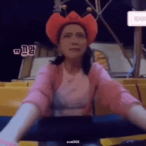 a woman wearing a pink shirt and a red cowboy hat is sitting in a chair at a carnival .
