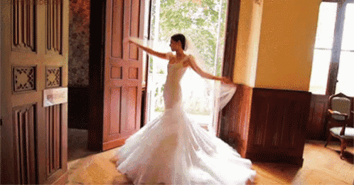 a bride in a wedding dress is dancing in a room with a door open .