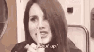 a woman is holding her finger to her lips and says `` shut up '' .