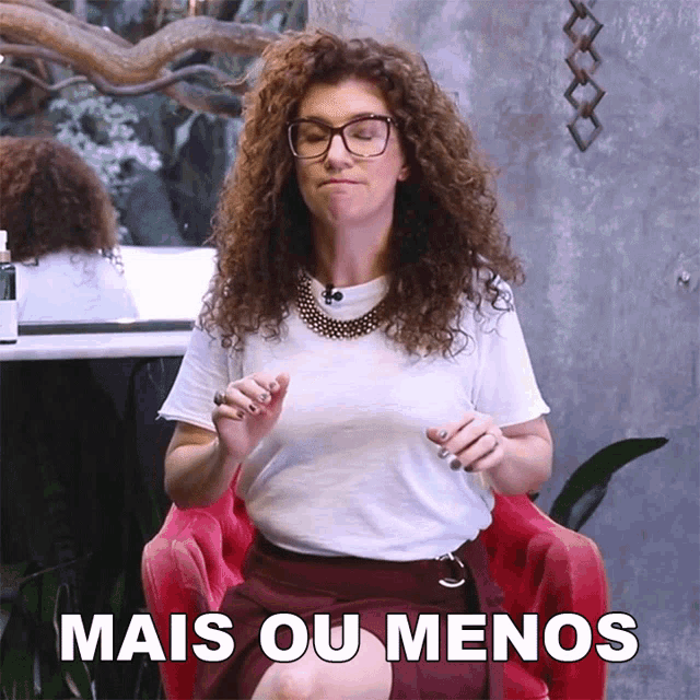 a woman with curly hair and glasses is sitting in a red chair with the words mais ou menos behind her