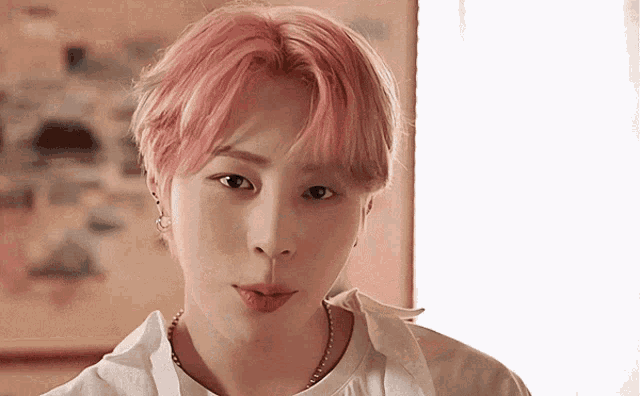 a young man with pink hair is looking at the camera