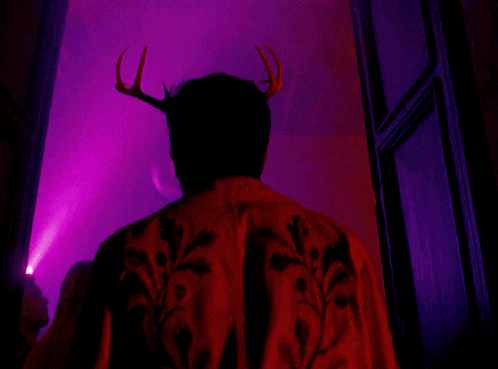 a man with antlers on his head is standing in front of a pink light