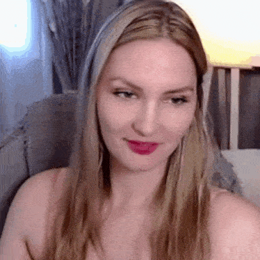a woman with long blonde hair and red lipstick is sitting in a chair and smiling .