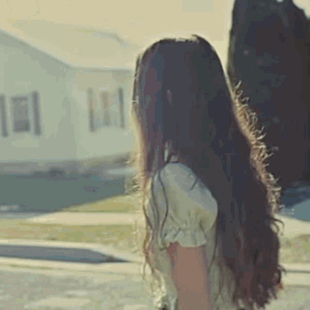 a woman with long hair is walking down the street in front of a white house .