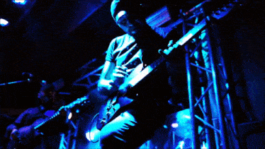 a man is playing a guitar in a dark room with blue lights