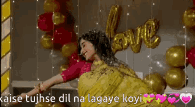 a woman in a yellow saree is dancing in front of balloons and a love sign .