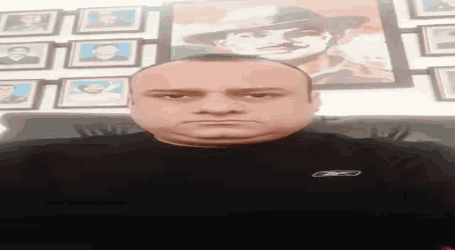 a man in a black shirt is sitting in front of a wall with pictures of soldiers on it .
