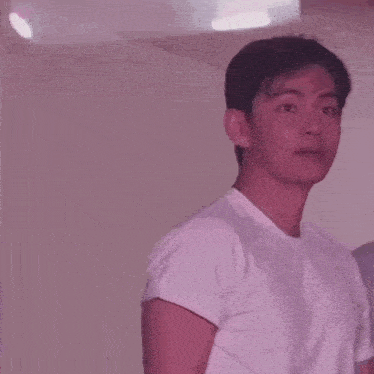 a young man in a white t-shirt is clapping his hands in a room .