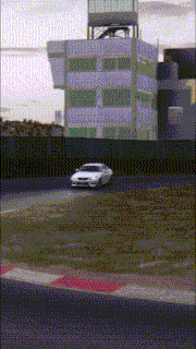a white car is driving down a race track with a building in the background