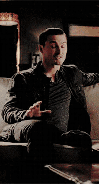 a man in a black jacket is sitting on a couch holding a glass