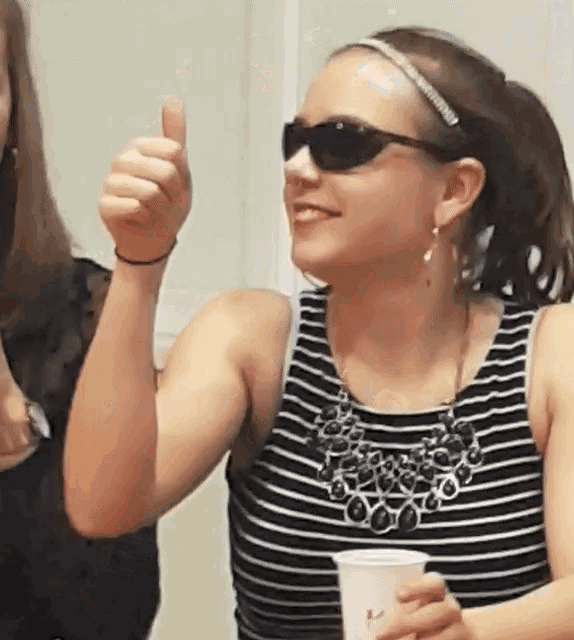 a woman wearing sunglasses gives a thumbs up while holding a cup