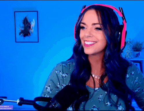 a woman wearing pink headphones and a green shirt smiles in front of a microphone