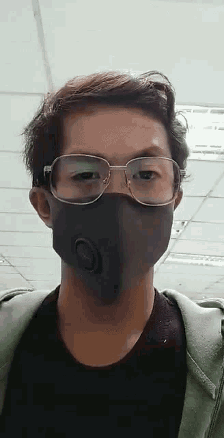 a young man wearing glasses and a mask is standing in front of a white ceiling .