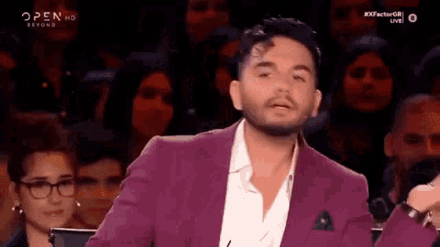 a man in a purple suit and white shirt is standing in front of a crowd .
