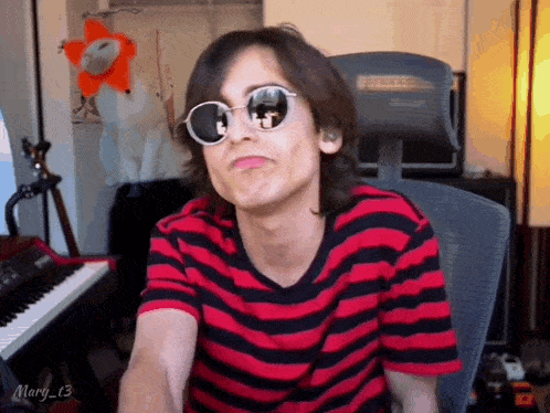 a man wearing sunglasses and a red and black striped shirt is sitting in a chair .