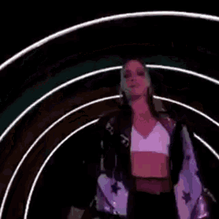 a woman in a crop top is dancing in a dark room with her arms outstretched .